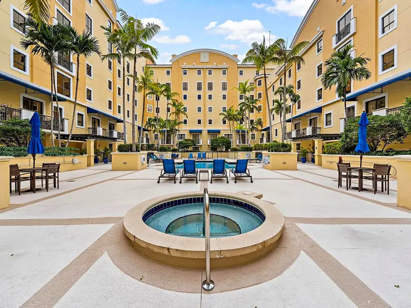 Pool courtyard and circular spa at The Colonnade, framed by yellow facades and palms.